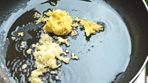 Place a pan on the heat and add 1 tbsp of sesame oil. To the pan, add the grated ginger and minced garlic and stir fry for a minute until the garlic is fragrant.