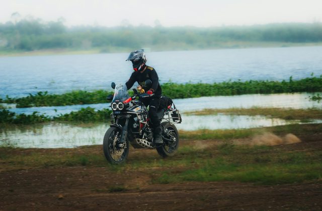 Motorcyclist riding on dirt near a body of water